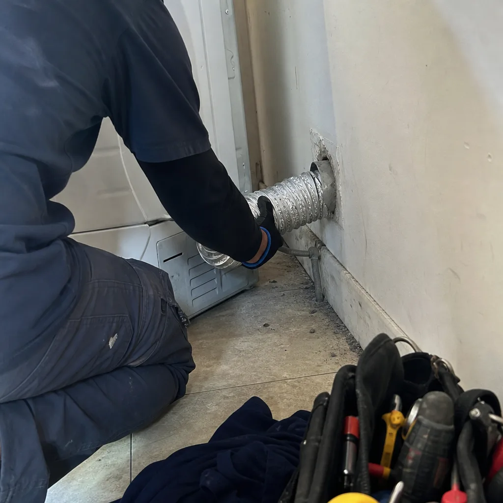 Technician connecting metallic dryer vent hose for maintenance and air duct cleaning